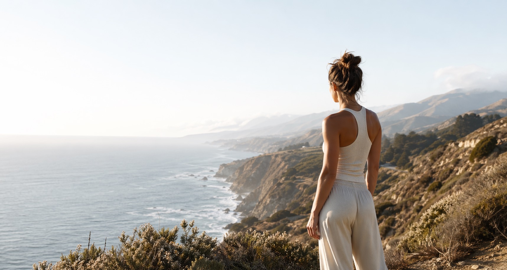 Woman with a messy bun standing on California cliffs overlooking the ocean.
